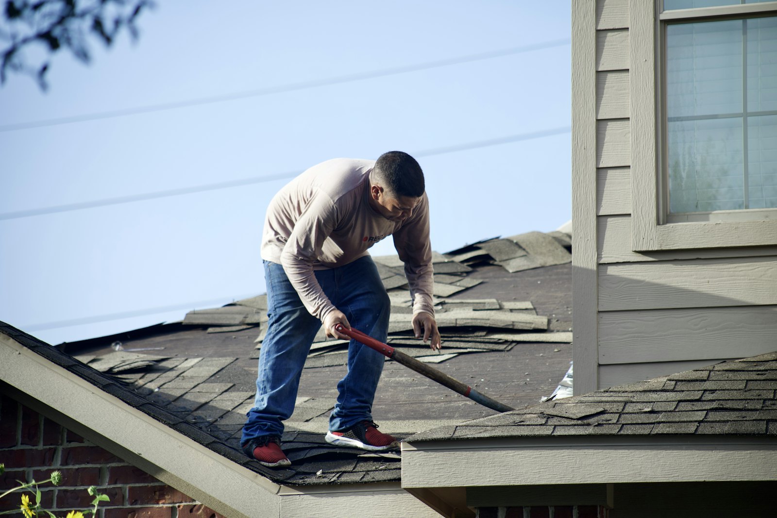 A roofer tearing old shingles off a house roof